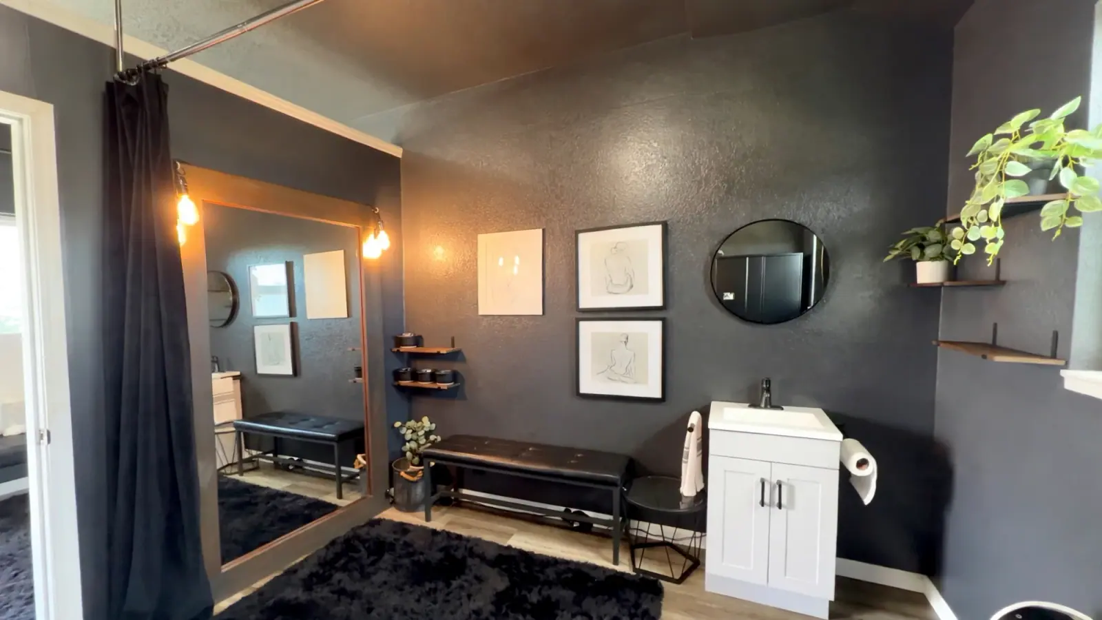 The deSoleil treatment room: charcoal textured walls, a tall mirror lit by warm bulbs, a black tufted bench, line-art prints and a white vanity