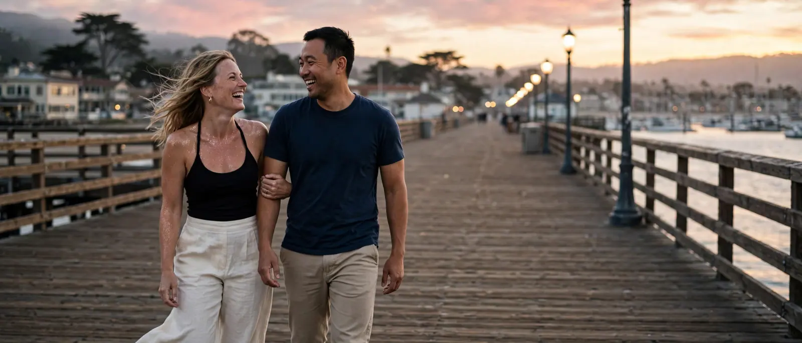 A couple walks arm in arm along the wharf at sunset