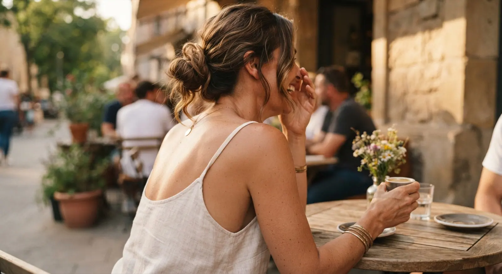 A woman with sun-warmed shoulders laughs over an espresso at a sidewalk cafe table