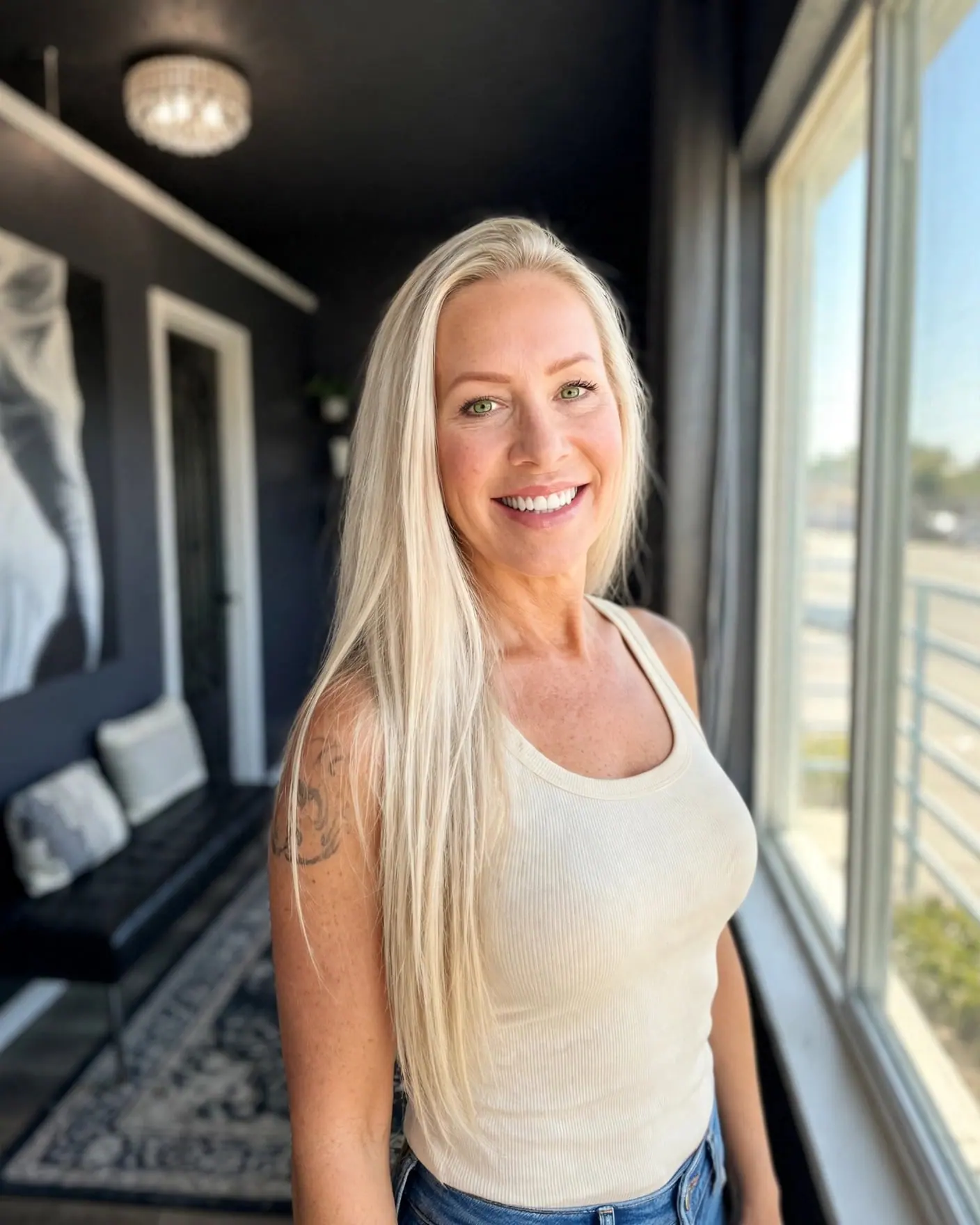 Jana smiles beside the big window of her charcoal-walled studio, ready to welcome you